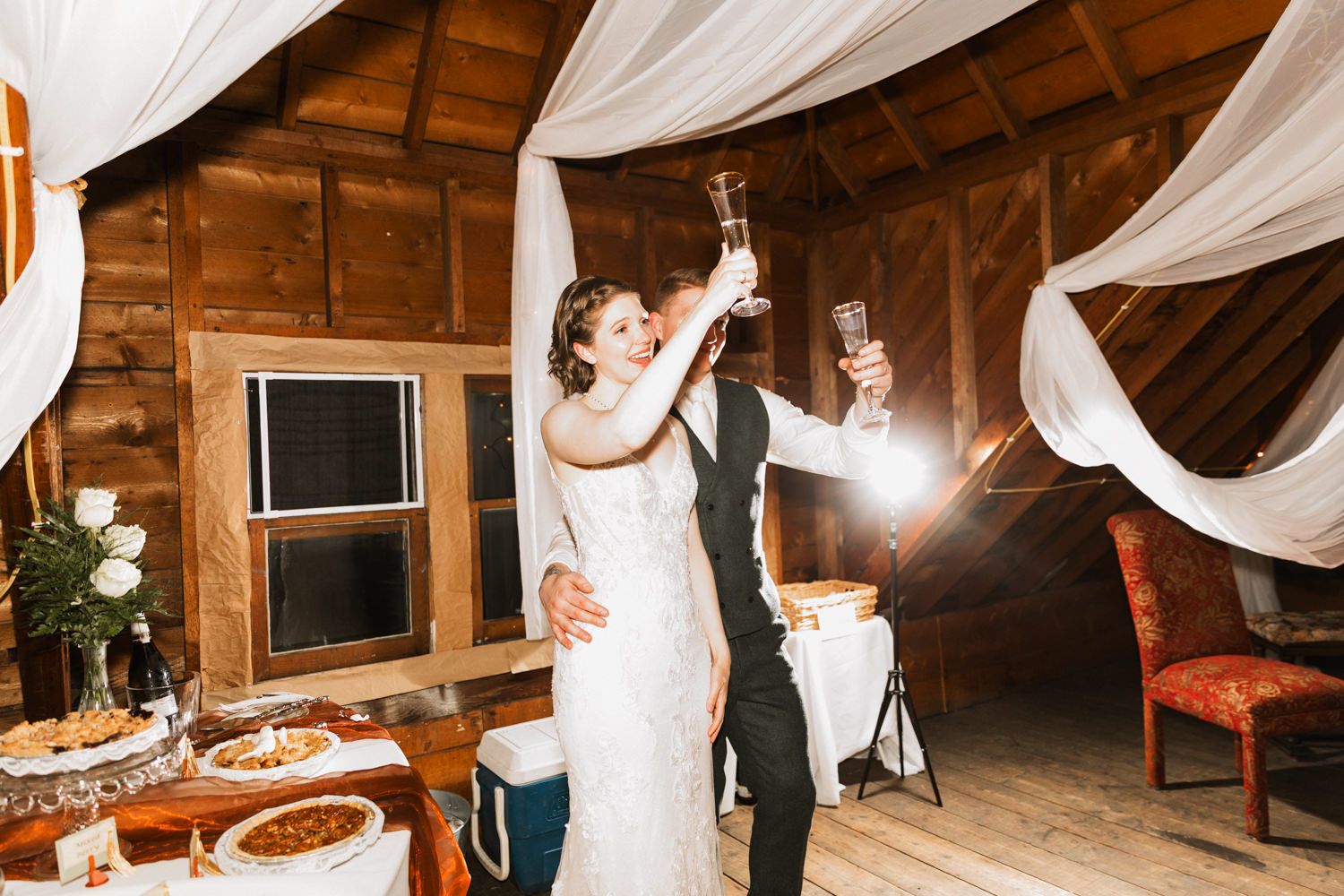 Rustic barn wedding reception with white draping and string lights creating a romantic ambiance.