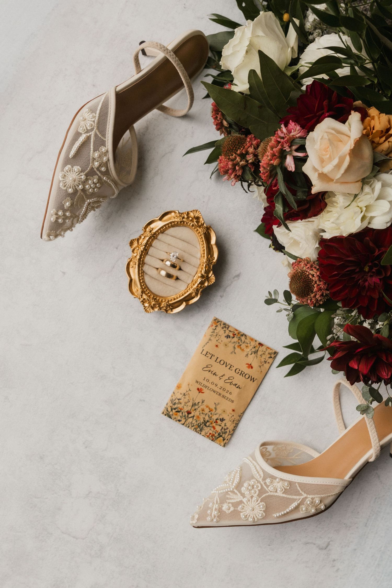 Wedding flat lay with lace embroidered bridal heels, a gold ring box, a Let Love Grow card and a burgundy and cream floral bouquet.