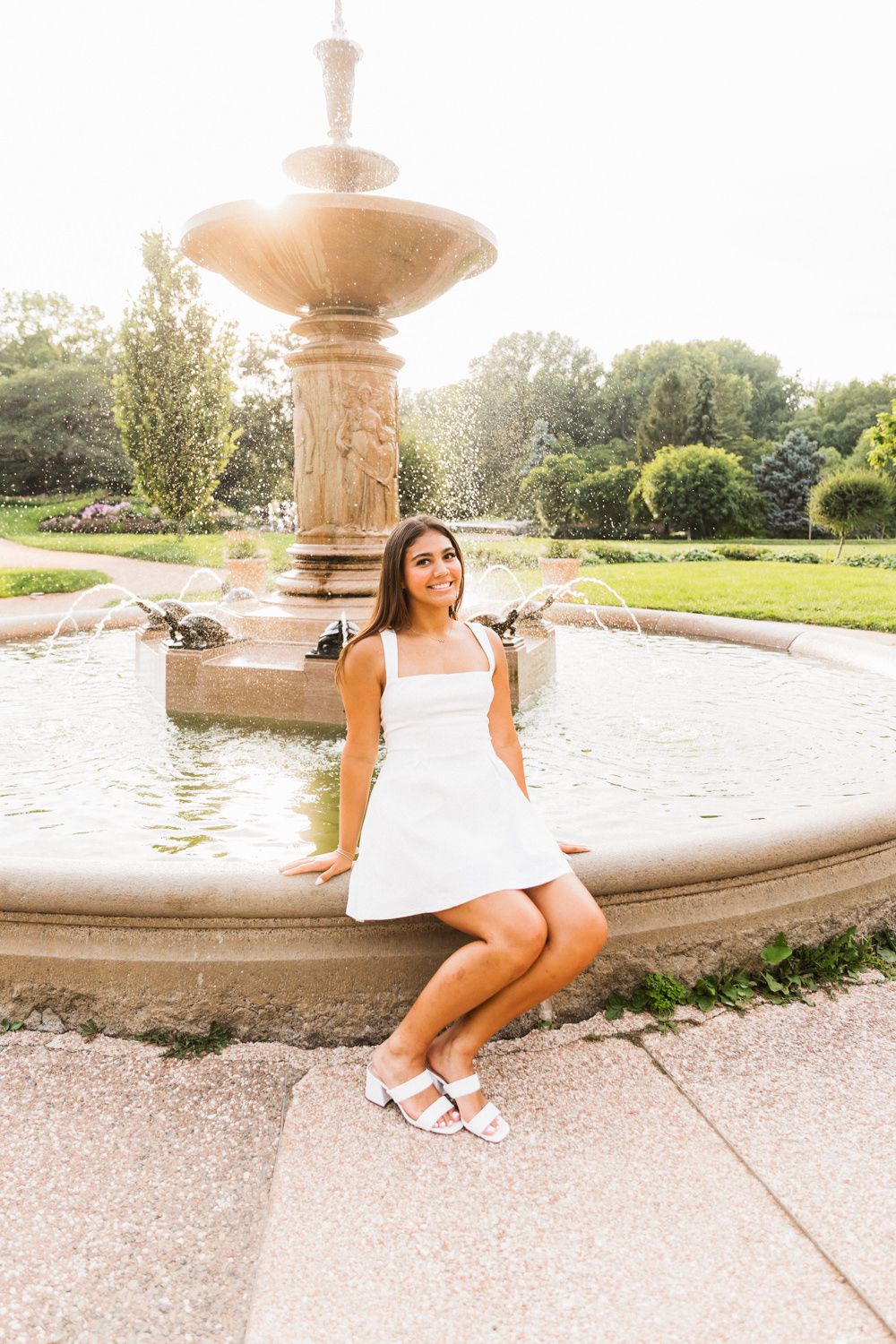 White sundress outfit by classic stone fountain in sunny garden setting.