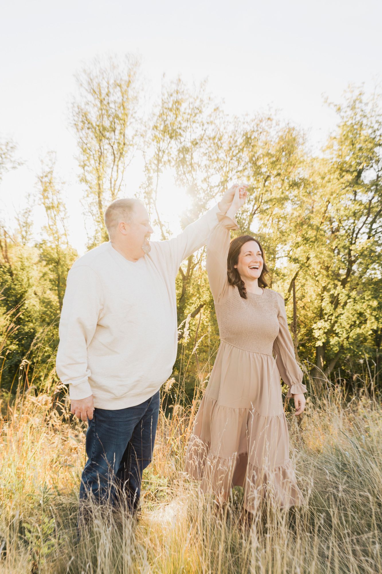 A couple enjoying a sunlit moment together in tall grass with golden trees in the background.