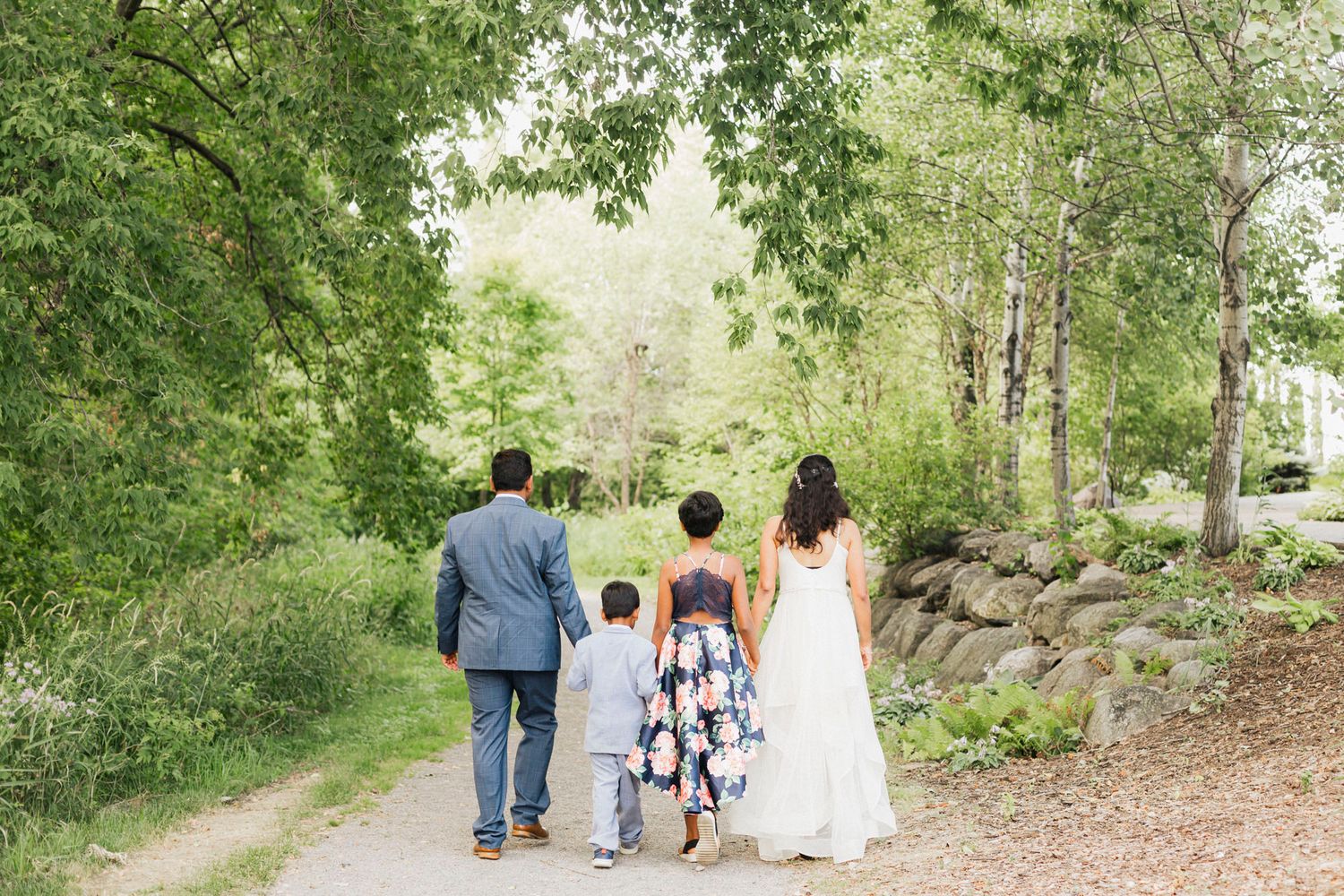 Family walking together on a tree-lined path during an outdoor photo session.