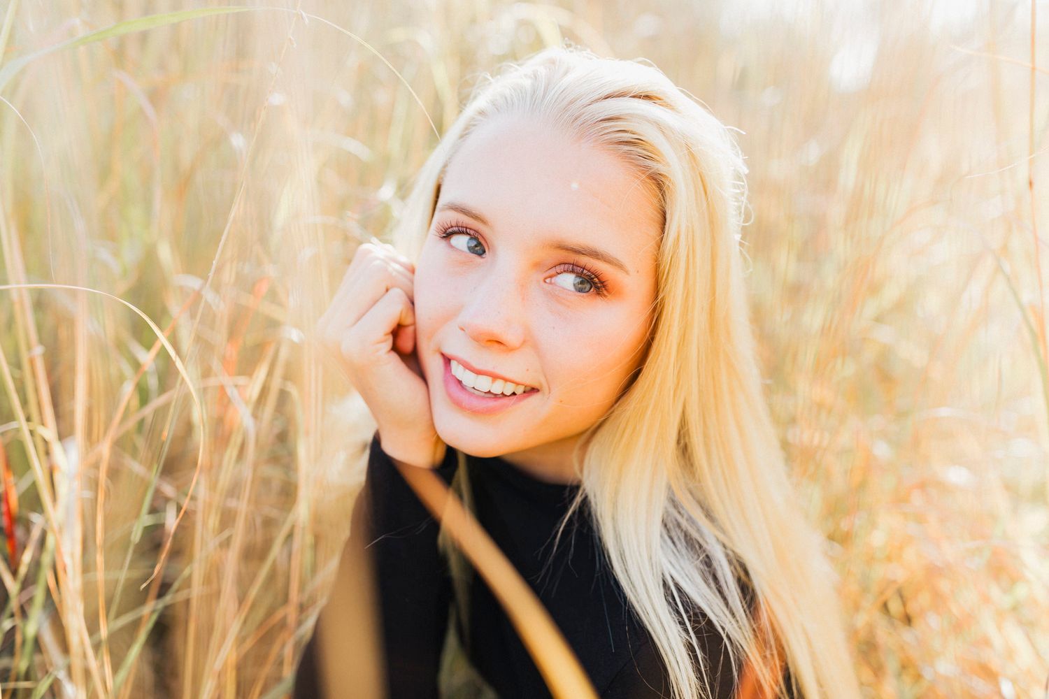 Sunny outdoor portrait of a blonde person smiling among tall grass.