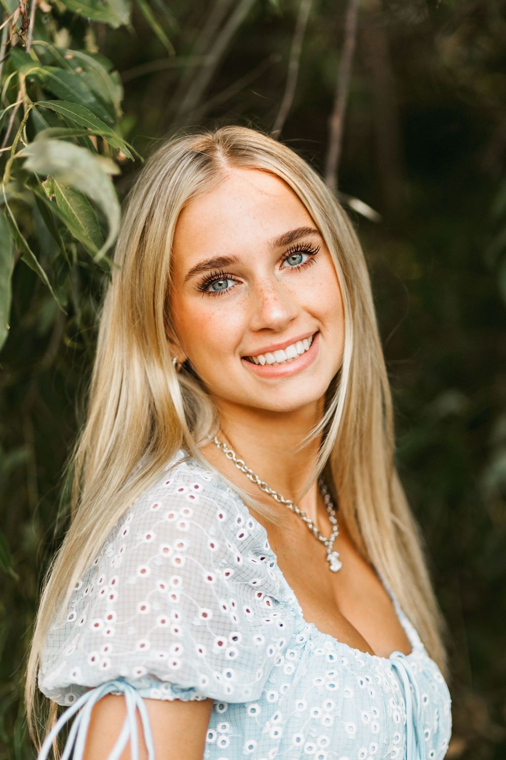 Side portrait showing eyelet dress detail and delicate jewelry against natural backdrop.