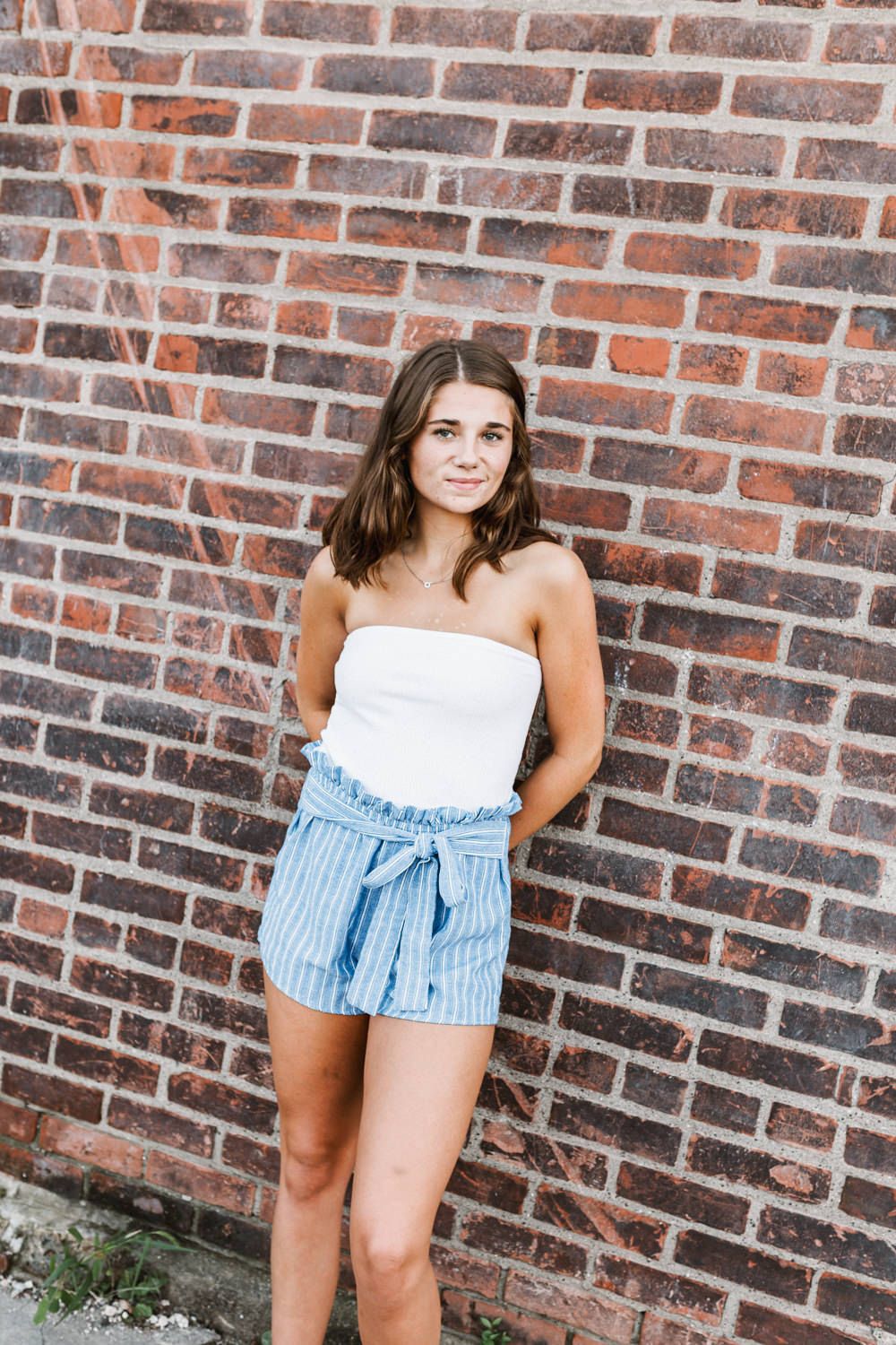 Portrait against brick wall wearing white top and blue striped shorts.