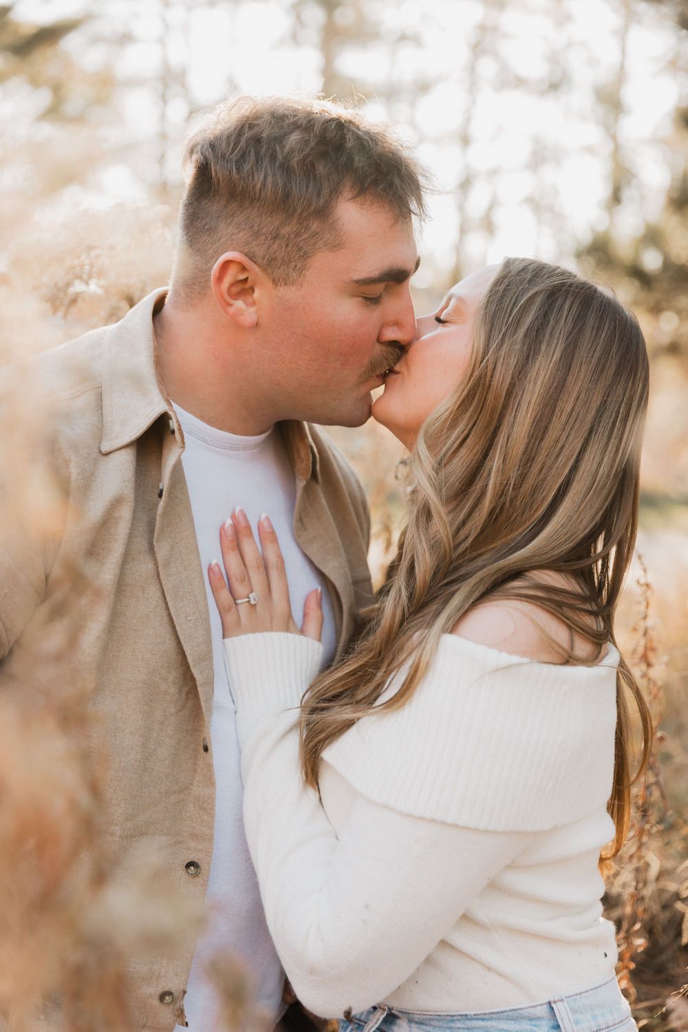 Intimate moment captured between a couple in white sweaters against a natural forest backdrop.