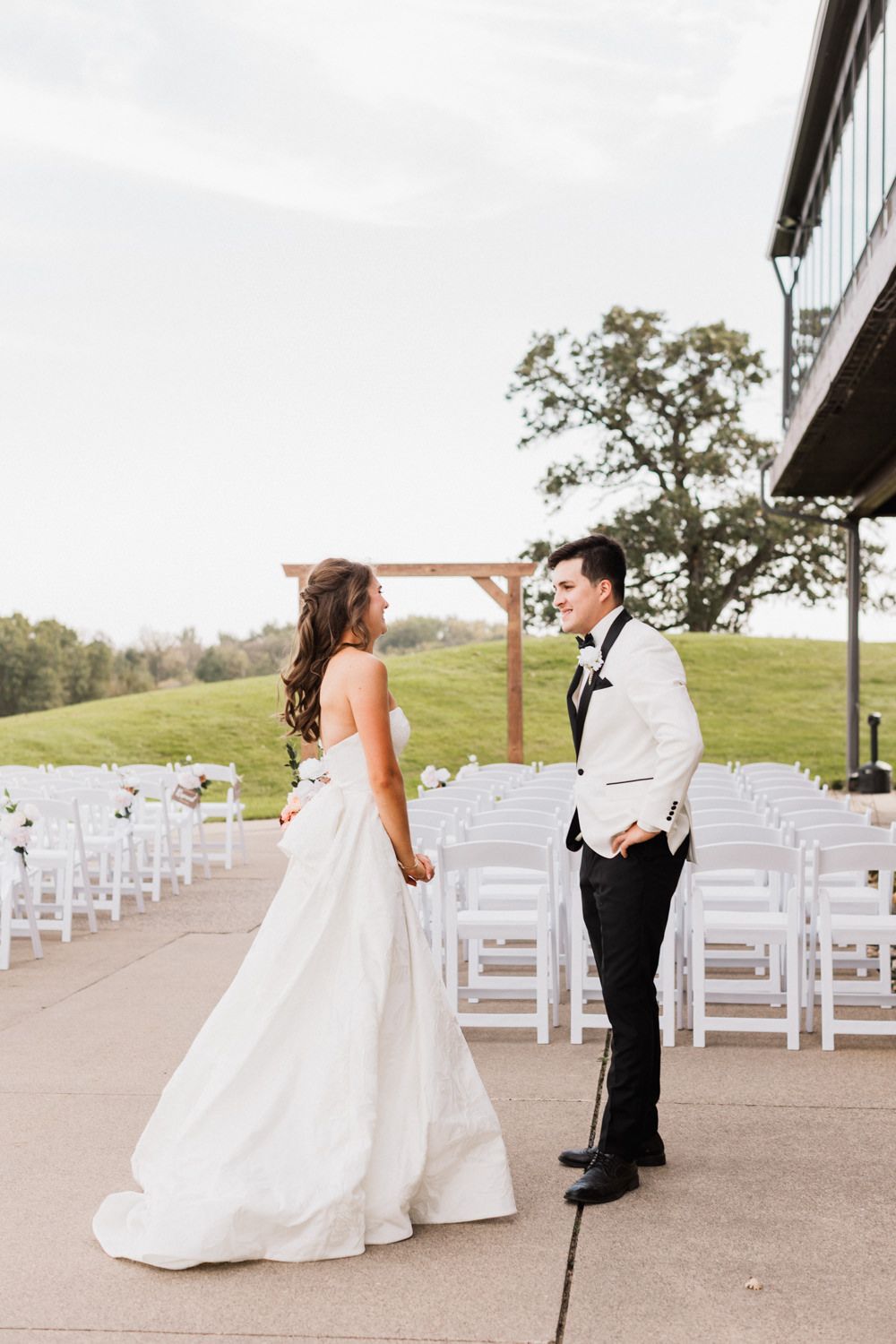 A series of first look photos showing a bride surprising her groom at an outdoor wedding venue with white chairs set up.
