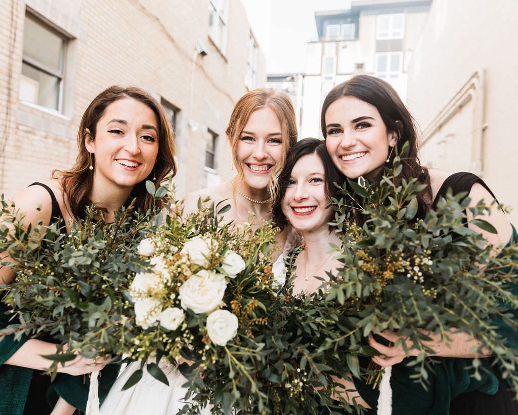 Bridesmaids holding elegant white and green floral bouquets pose together in winter.