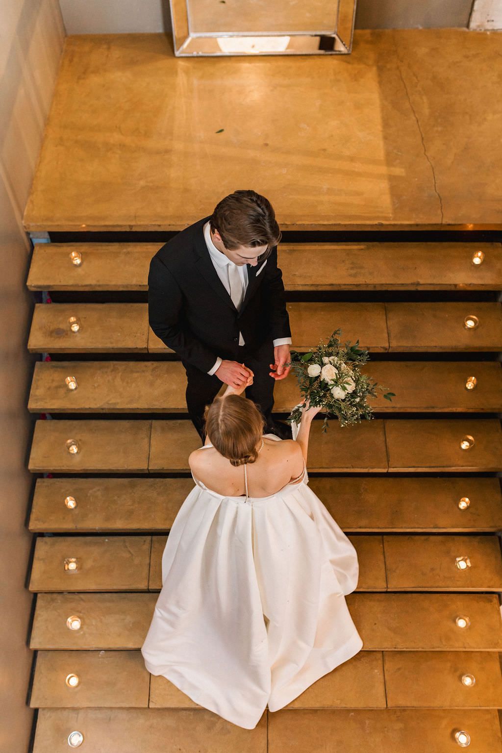Wedding couple dances on wooden steps illuminated by string lights in a romantic venue setting.