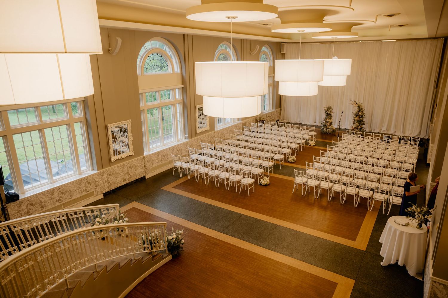 Elegant wedding venue with white chairs arranged in rows under large pendant lights in a grand ballroom.