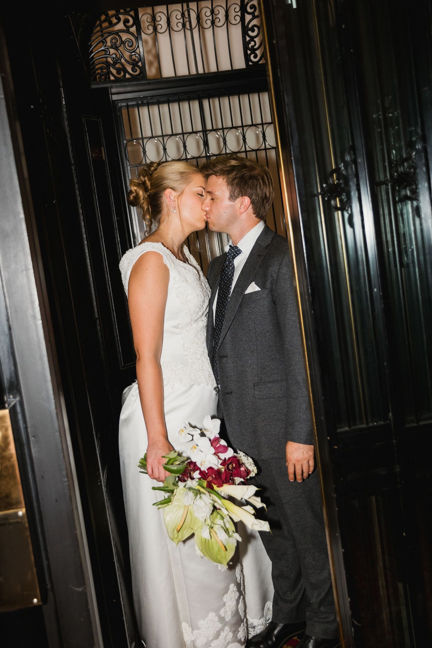 Bride and groom share a romantic kiss in a wedding portrait, bride holding a bouquet of white and red flowers.
