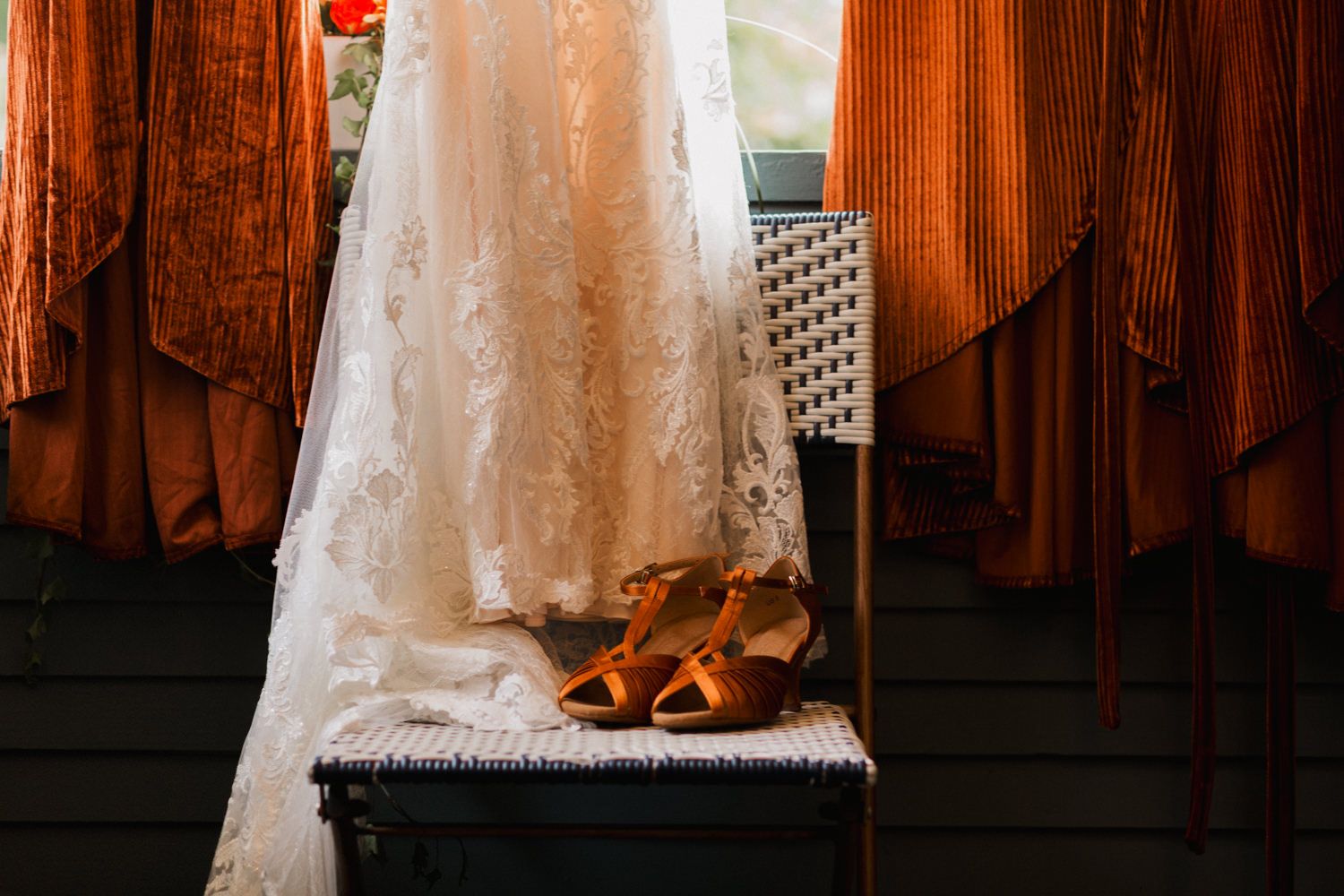 White wedding dress hanging in a rustic wooden room with natural light streaming through windows.