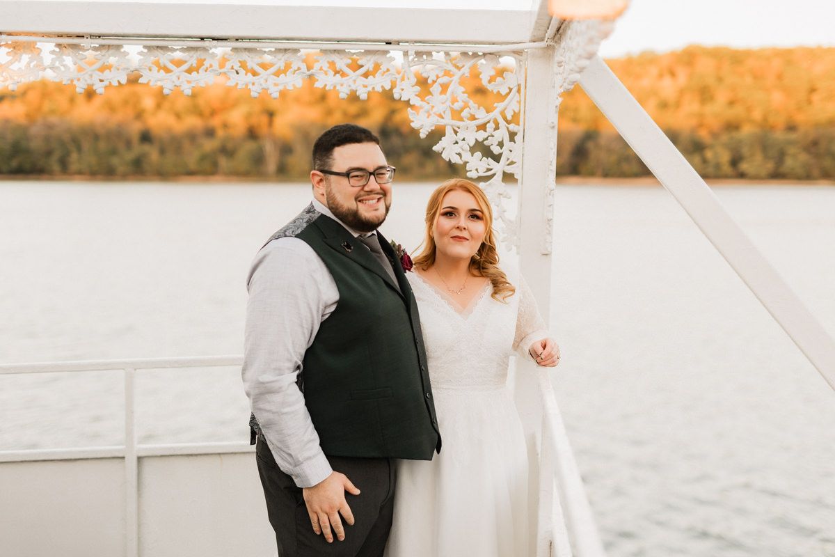 Newlyweds share a happy moment on a boat dock during golden hour with autumn colors in the background.