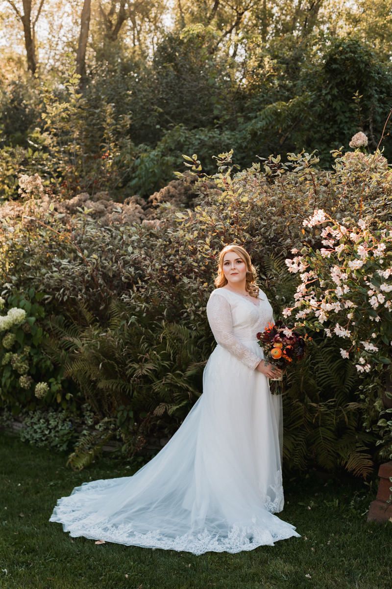An elegant bridal portrait in a garden setting with white lace gown and autumn-colored floral decorations.