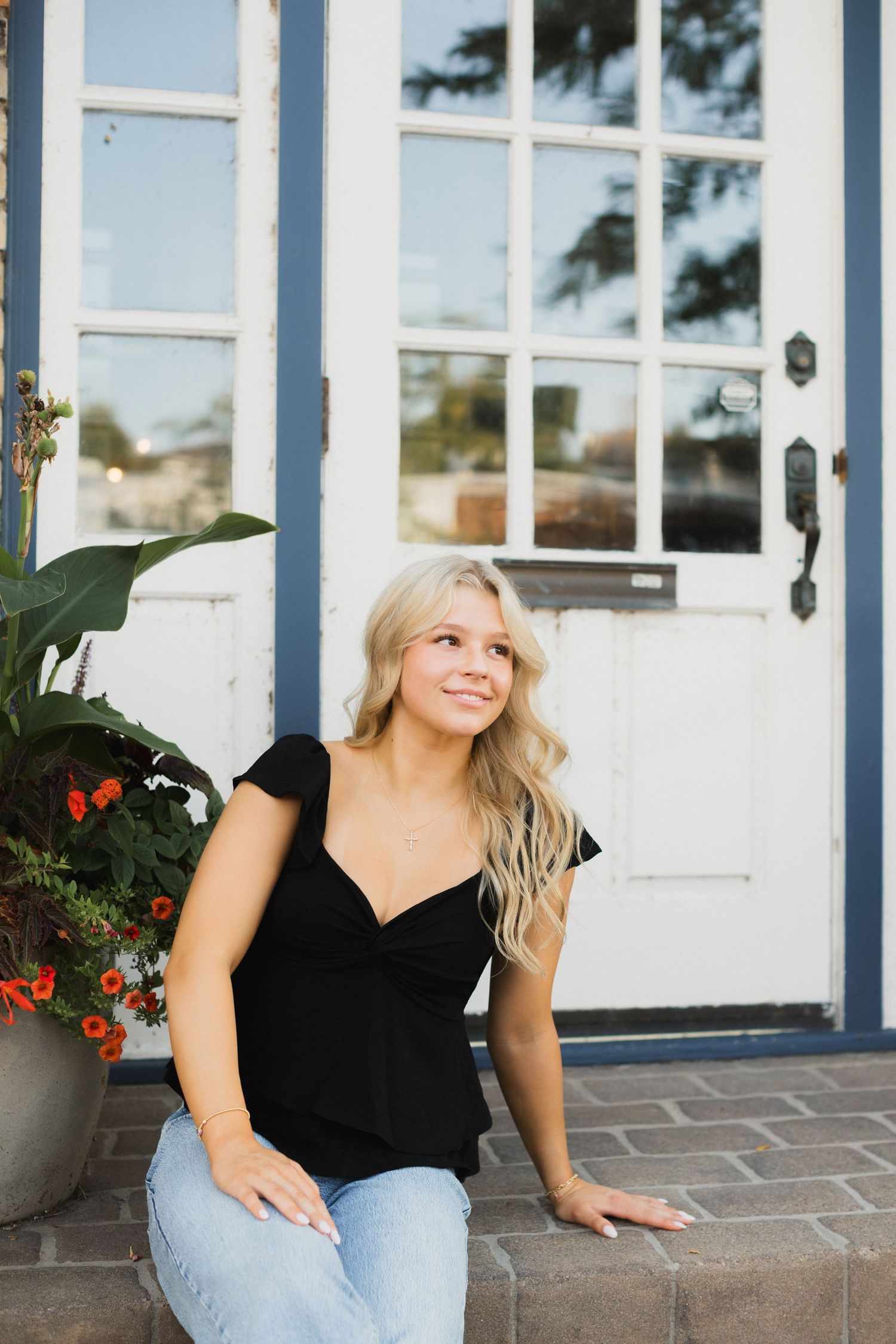 Young blonde woman in black top and jeans sitting on front porch steps, smiling outdoors.