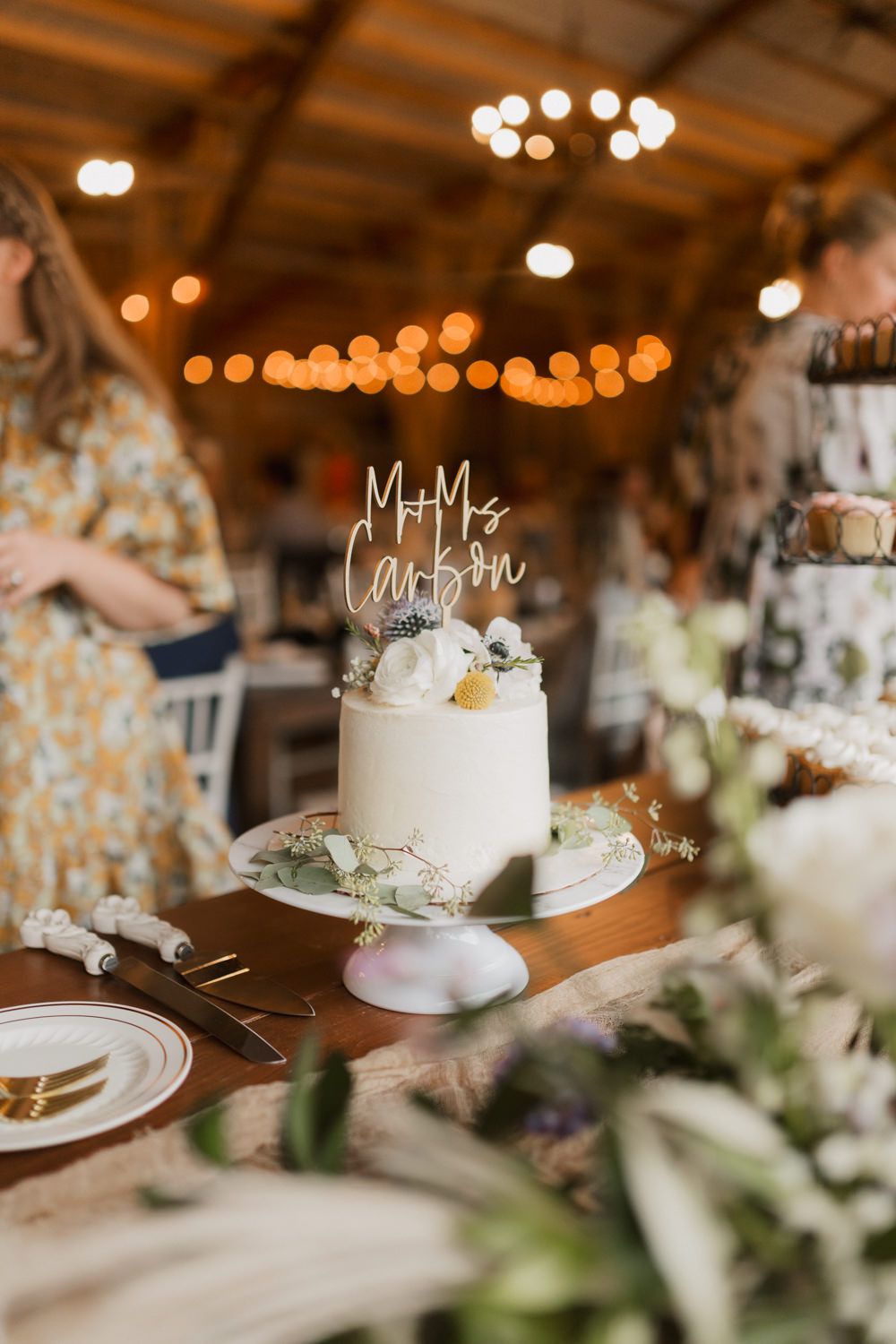 Elegant white wedding cakes displayed on stands with rustic decor and string lights in a romantic reception setting.