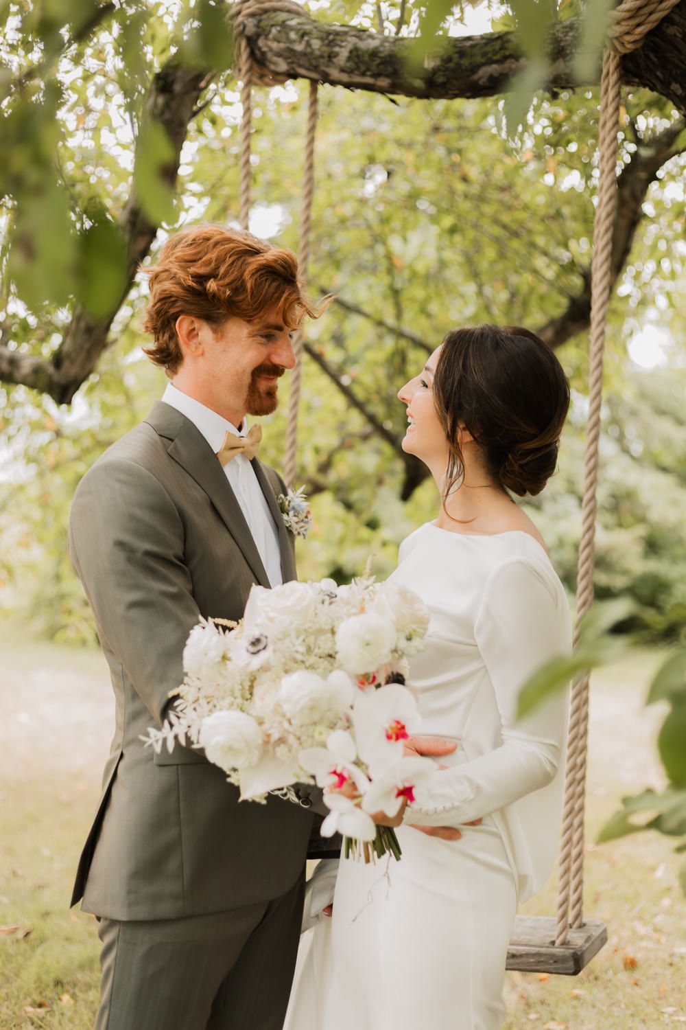 A romantic wedding moment captured outdoors with a white bouquet and natural greenery in the background.