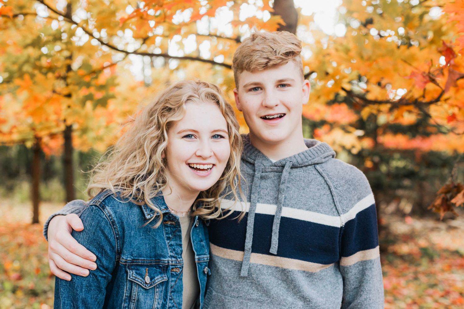 A couple stands together outdoors with vibrant orange autumn foliage in the background.