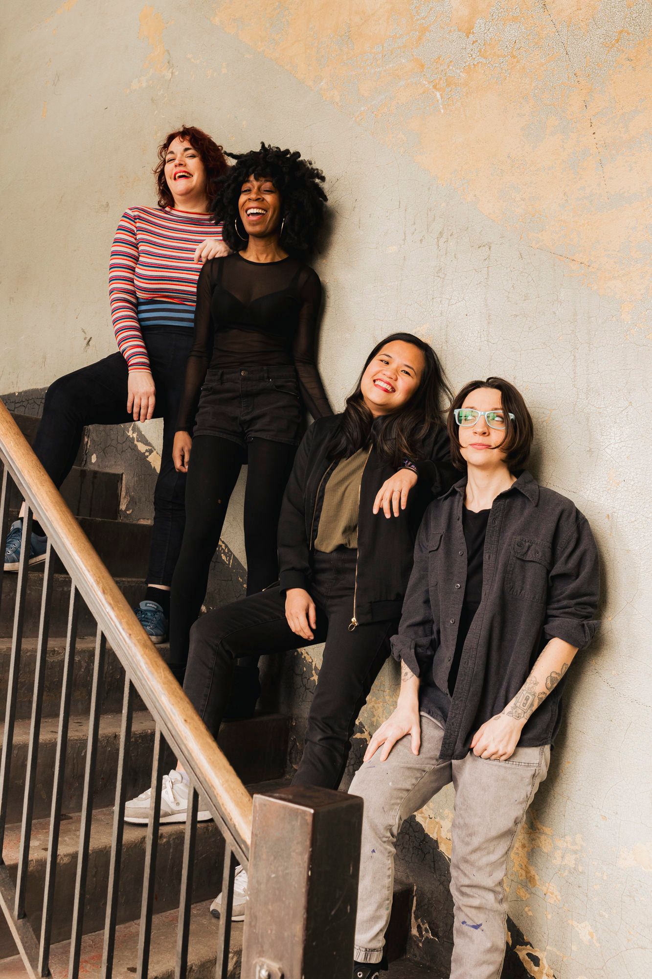 Group of four friends posing casually on staircase against textured wall.