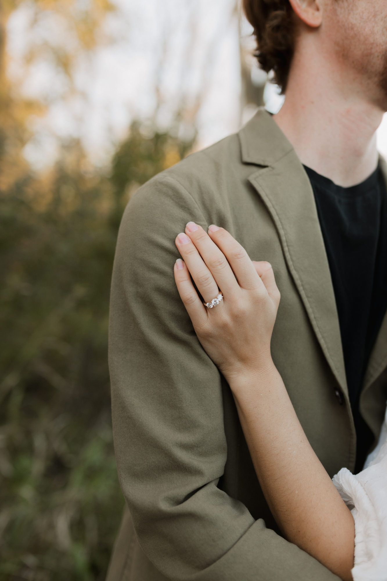 Close-up of a woman's hand with engagement ring resting on man's olive green blazer.