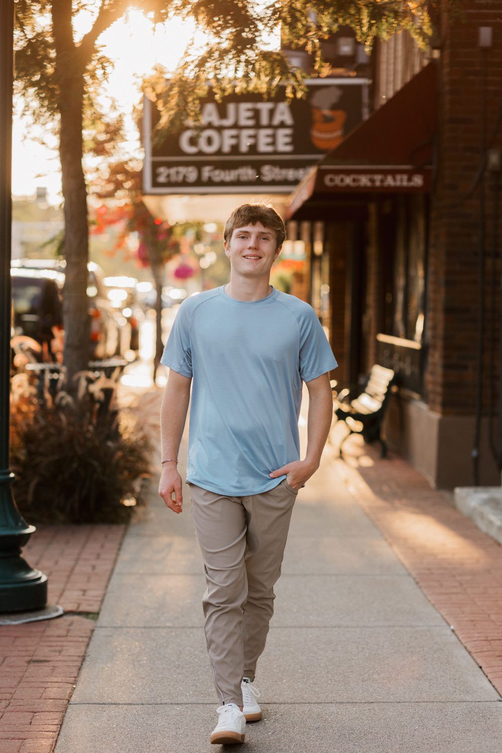 Light blue t-shirt and gray pants against an urban storefront with warm evening sunlight.