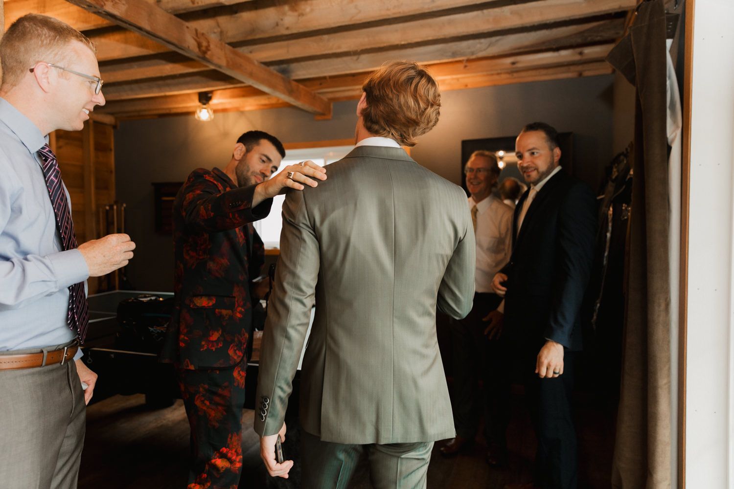 A group of people gather in a dimly lit room wearing suits and formal attire during what appears to be a social event.
