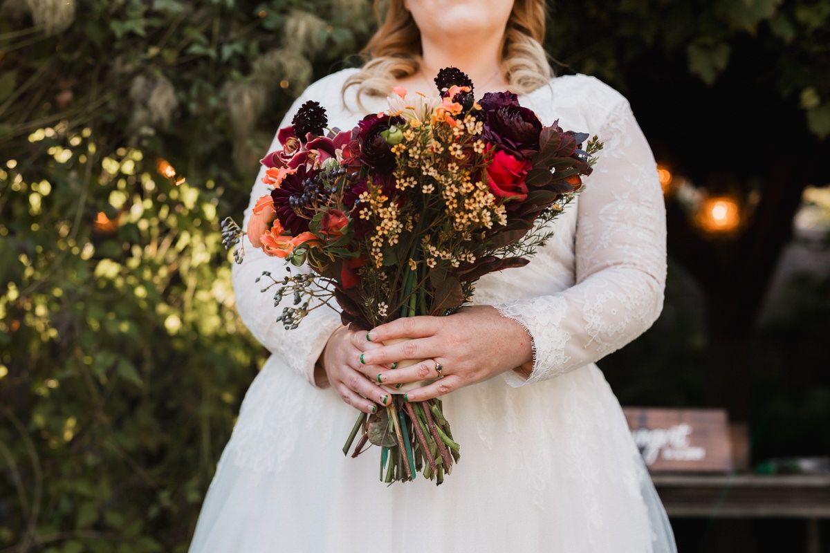 Autumn wedding bouquet featuring rich burgundy and orange blooms with greenery.