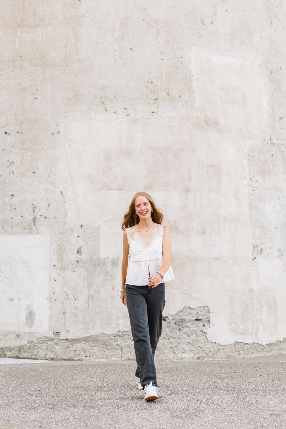 A casual streetwear look with a white sleeveless top and dark denim jeans styled with athletic sneakers.