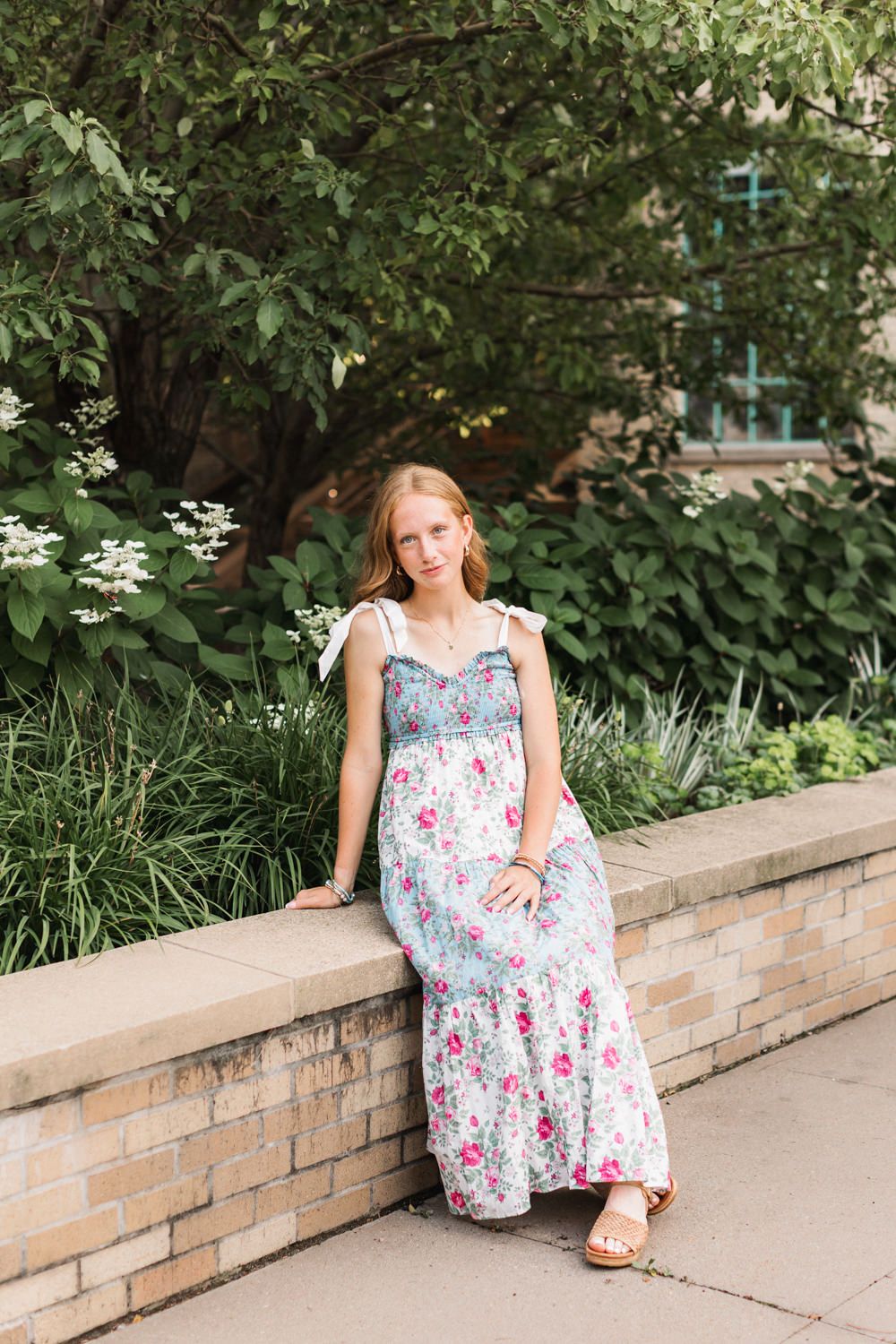 A floral summer dress is shown against a garden backdrop with stone retaining wall and greenery.