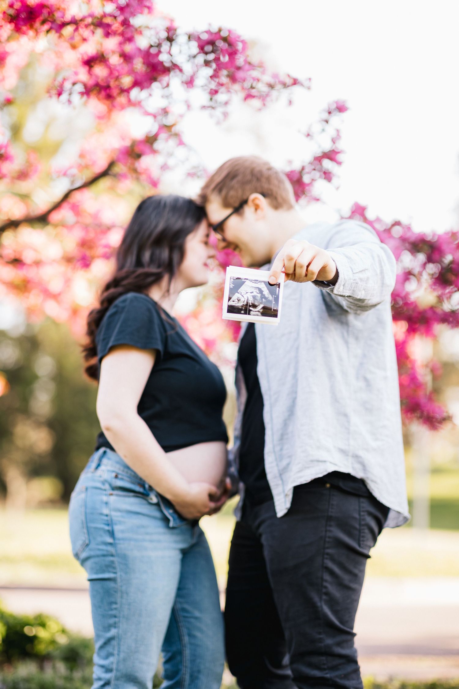 Couple shares ultrasound photo under pink flowering tree.