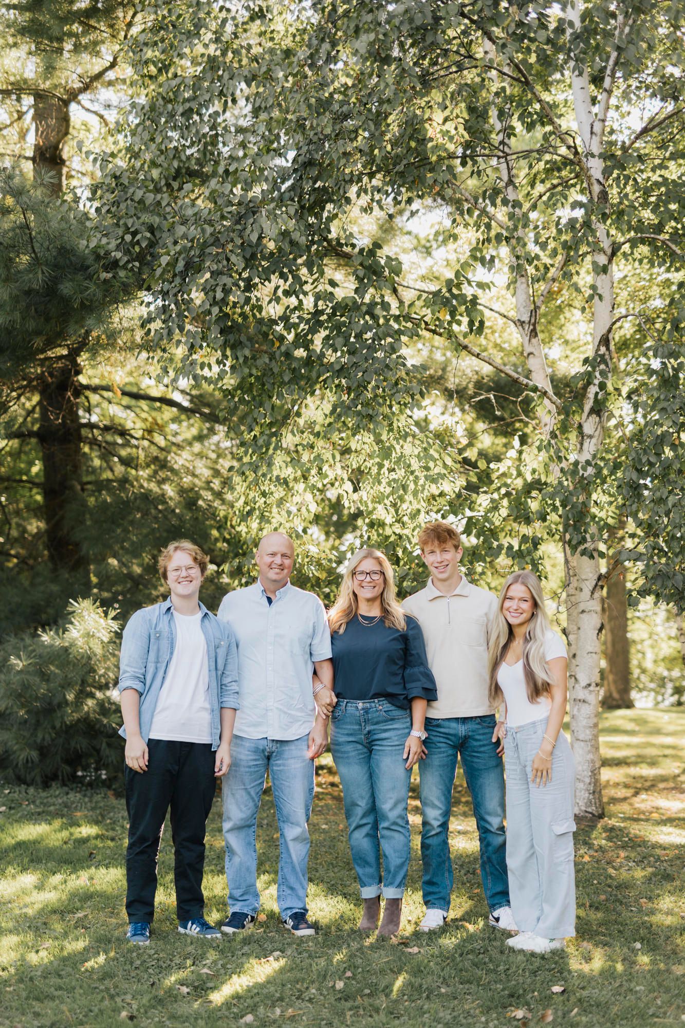 Large family group poses together under tree canopy for outdoor portrait session.