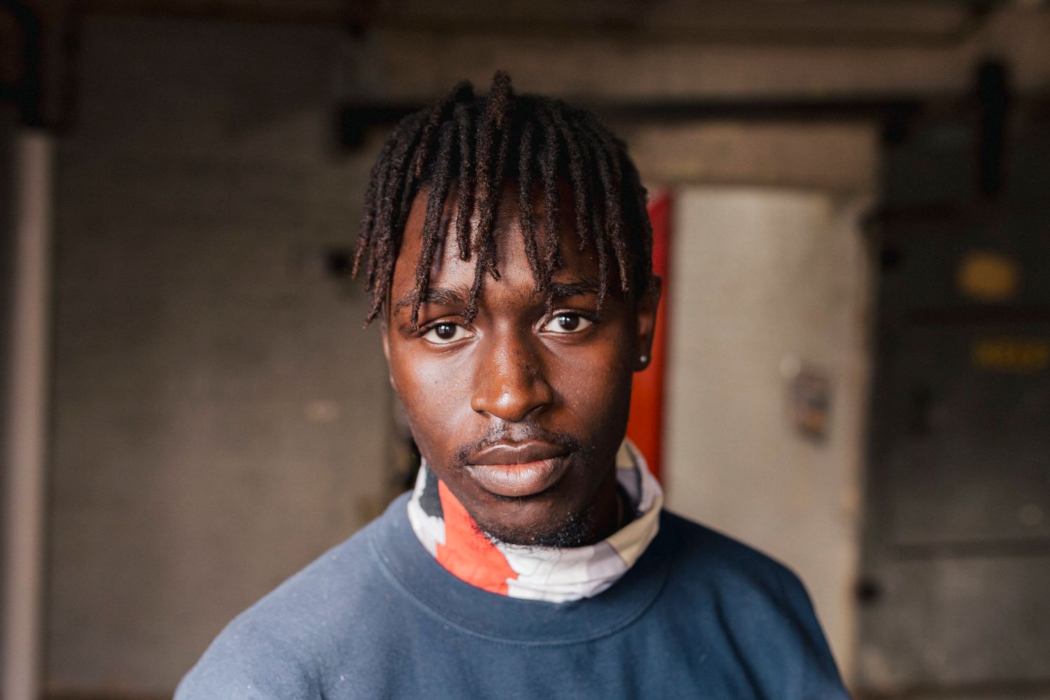 Portrait of person in blue sweater with braided hair against neutral background.