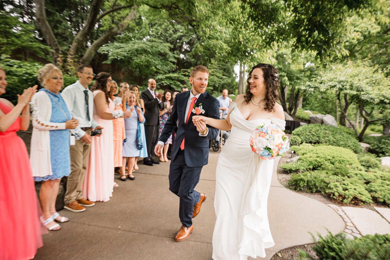 Wedding party walks along garden path while celebrating the newlyweds.