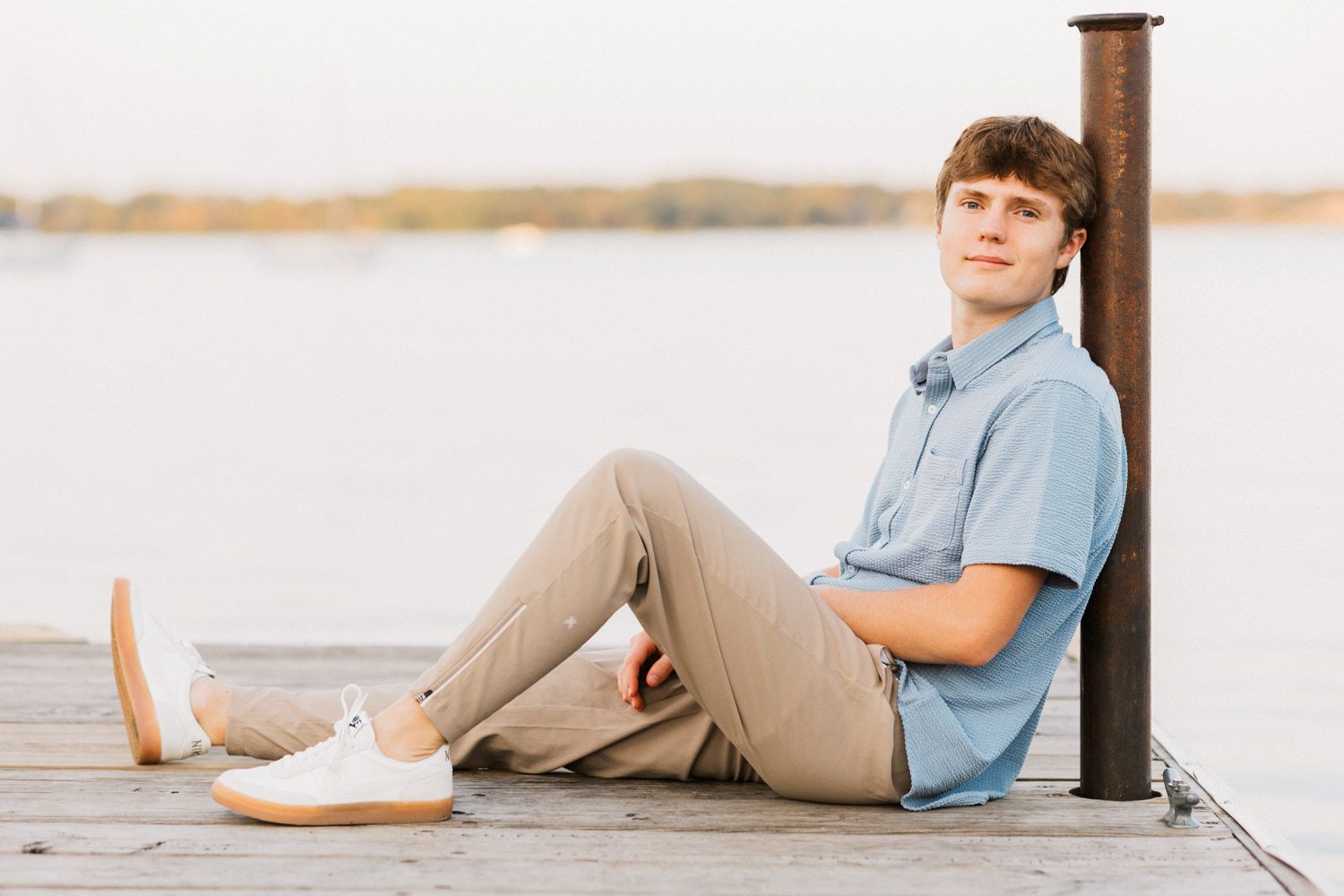 Person relaxing on wooden dock by calm lake waters at sunset.