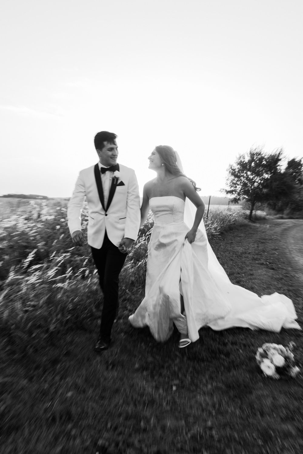A bride and groom run playfully through a grassy field in a series of artistic black and white wedding photographs.
