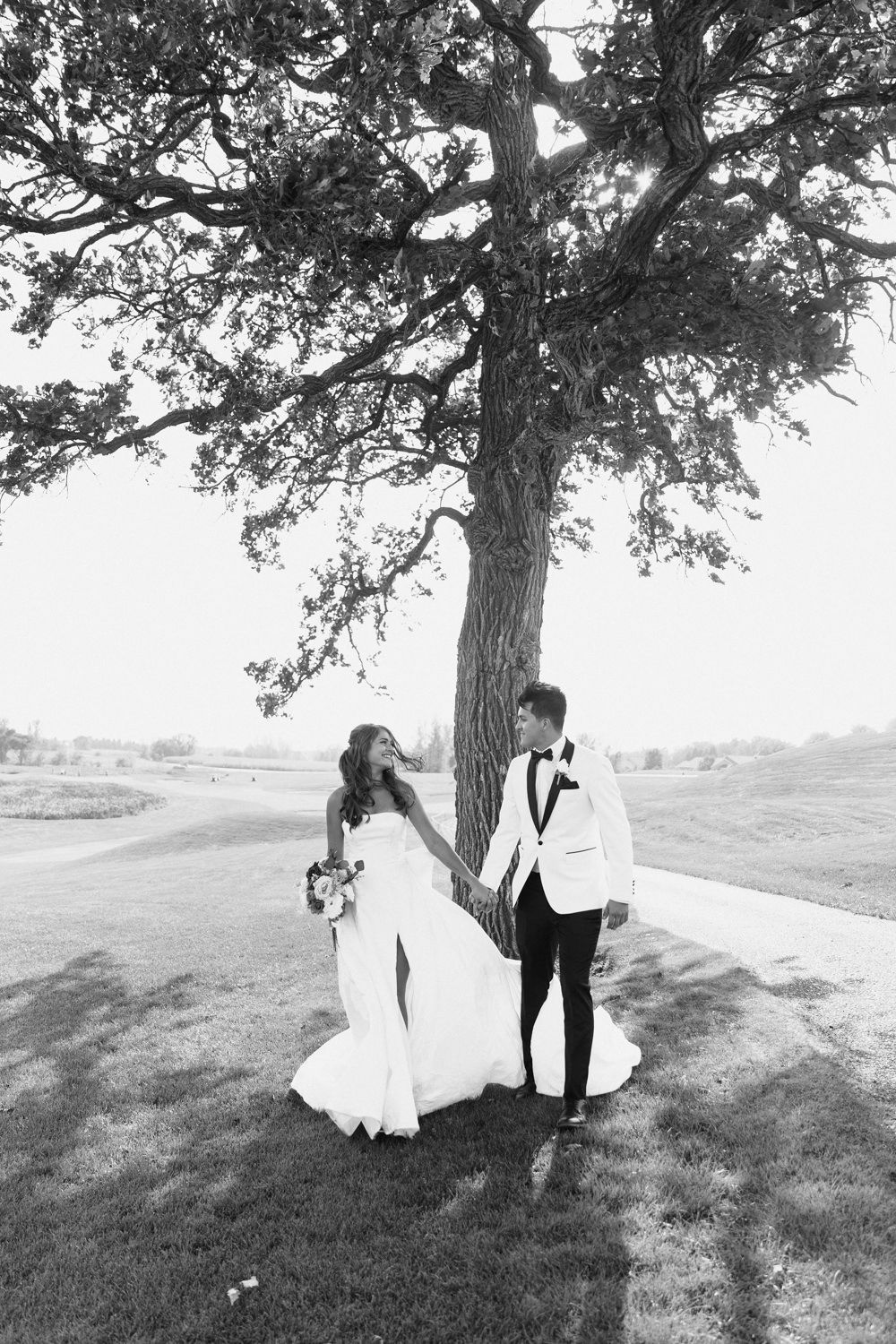Black and white wedding photos show a couple in romantic poses under a large tree in a scenic outdoor setting.