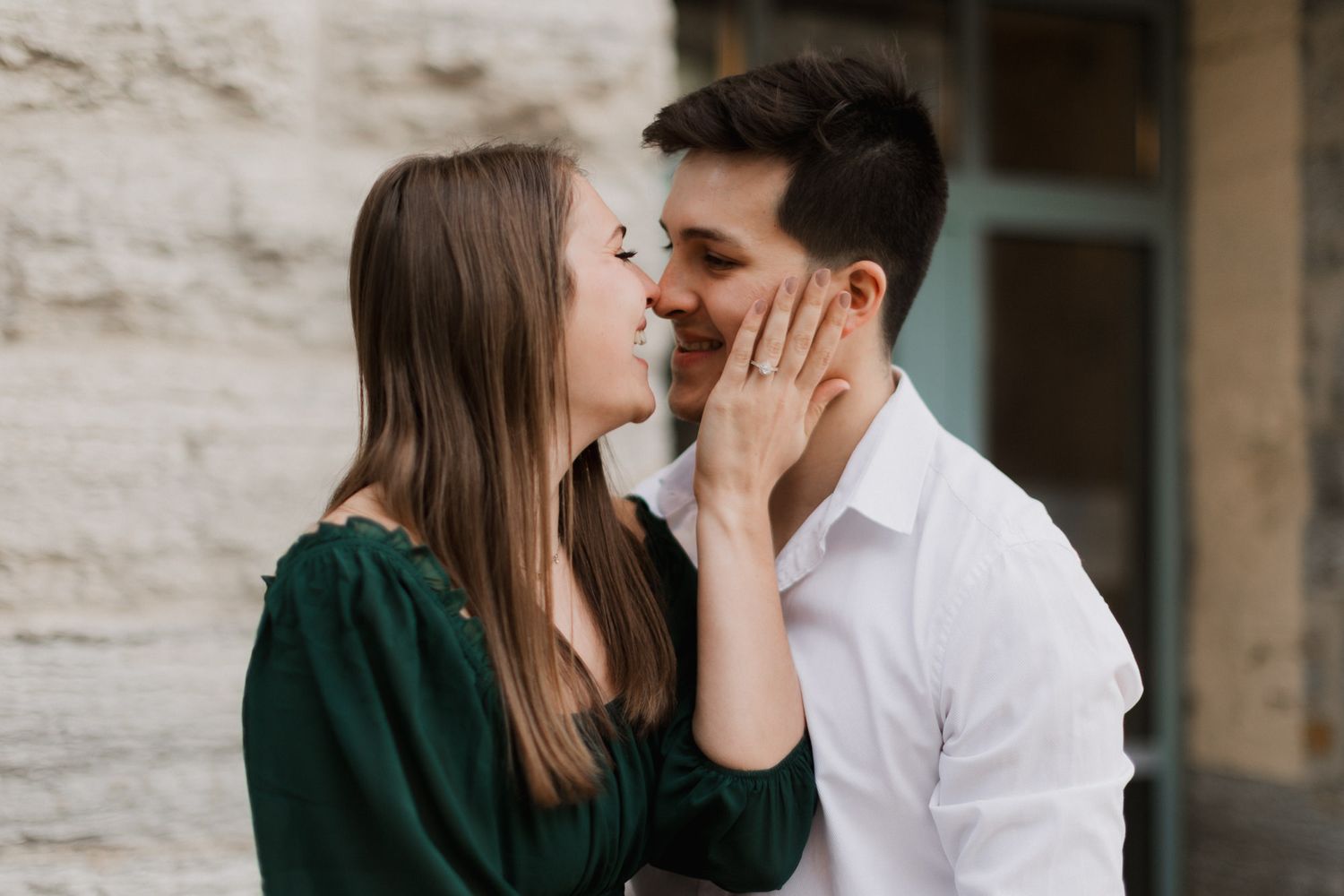 A romantic couple shares an intimate moment, woman in green top gently touching mans face as they lean in to kiss.