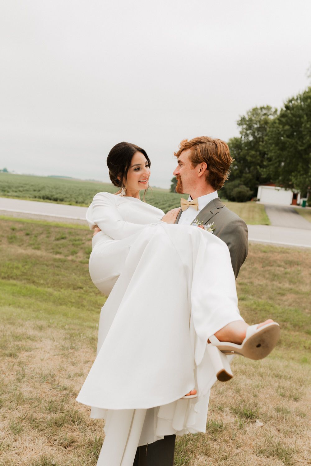A couple shares a joyful moment on a grassy hillside with flowing white fabric in the breeze.