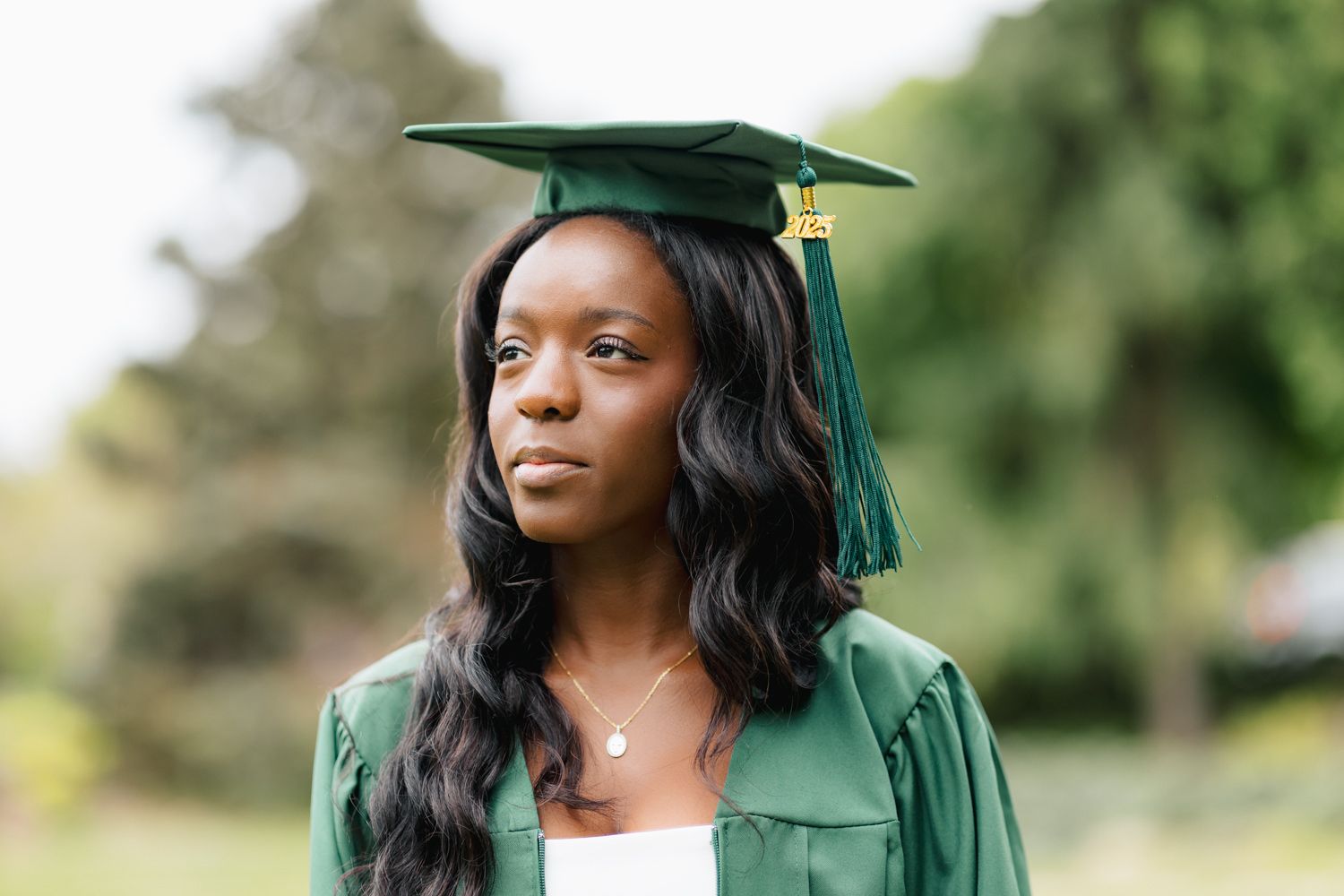 Graduate wearing emerald green graduation regalia in outdoor setting.