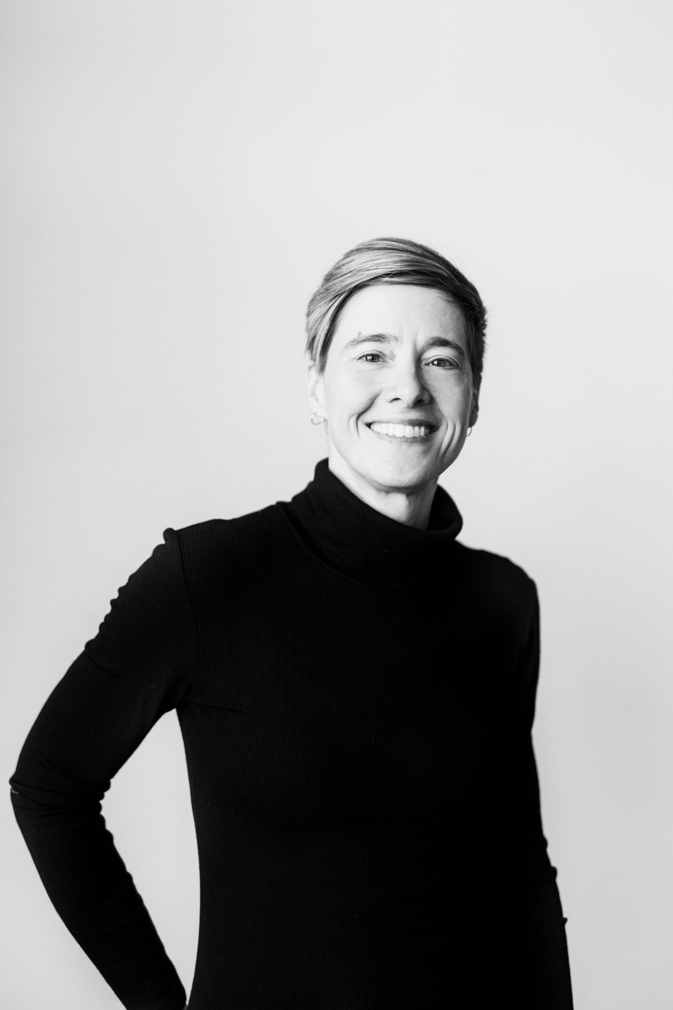 Black and white portrait of person in black turtleneck smiling against light background.