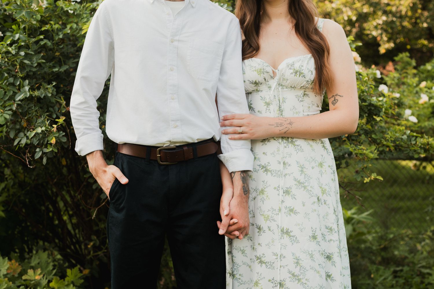 Couple holding hands in a garden, man in white shirt and black pants, woman in floral strapless dress.