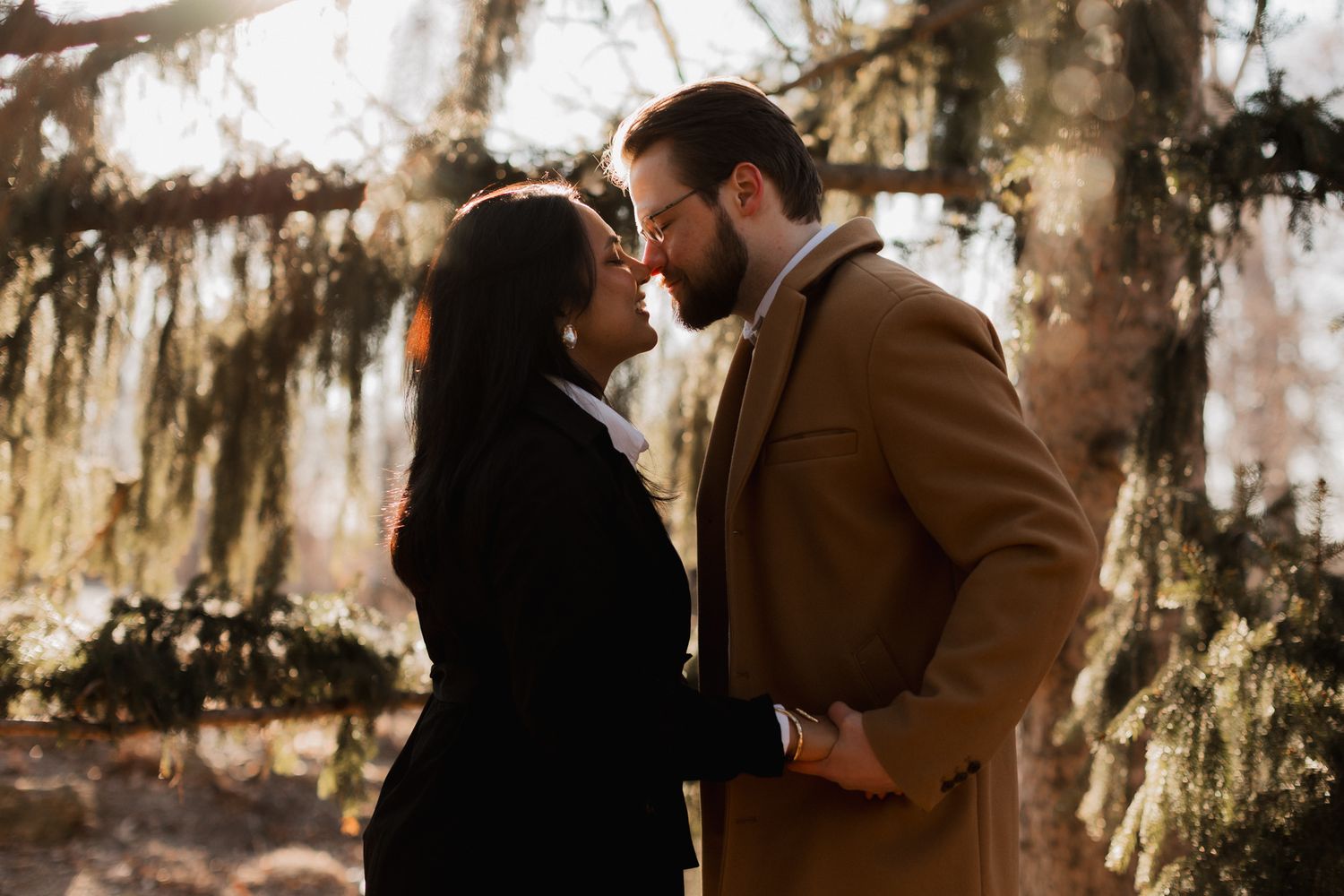 Romantic couple in elegant coats sharing an intimate moment under Spanish moss-draped trees.