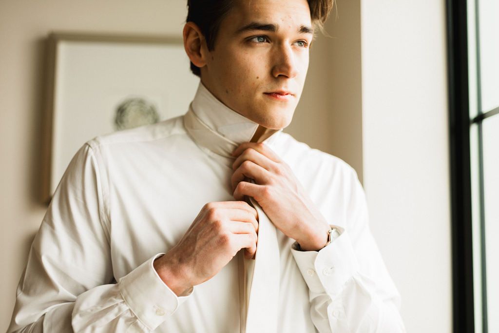 Person in white high-neck top poses thoughtfully by window in bright natural light.