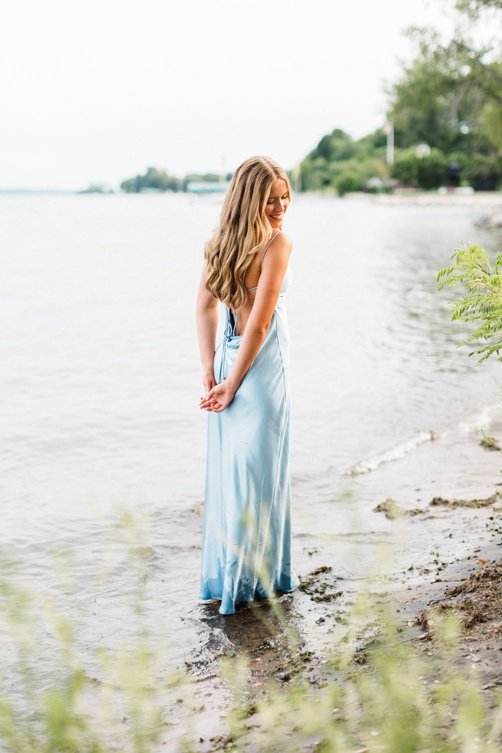 Serene waterfront scene with flowing blue dress and natural shoreline.