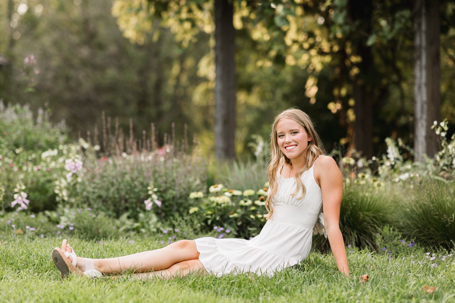 Person in white dress relaxes on grassy garden ground surrounded by summer wildflowers.