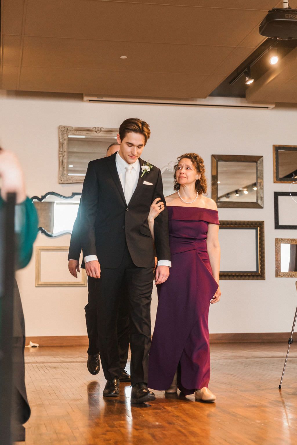 A couple walking arm in arm at a wedding reception with framed mirrors on the wall behind them.