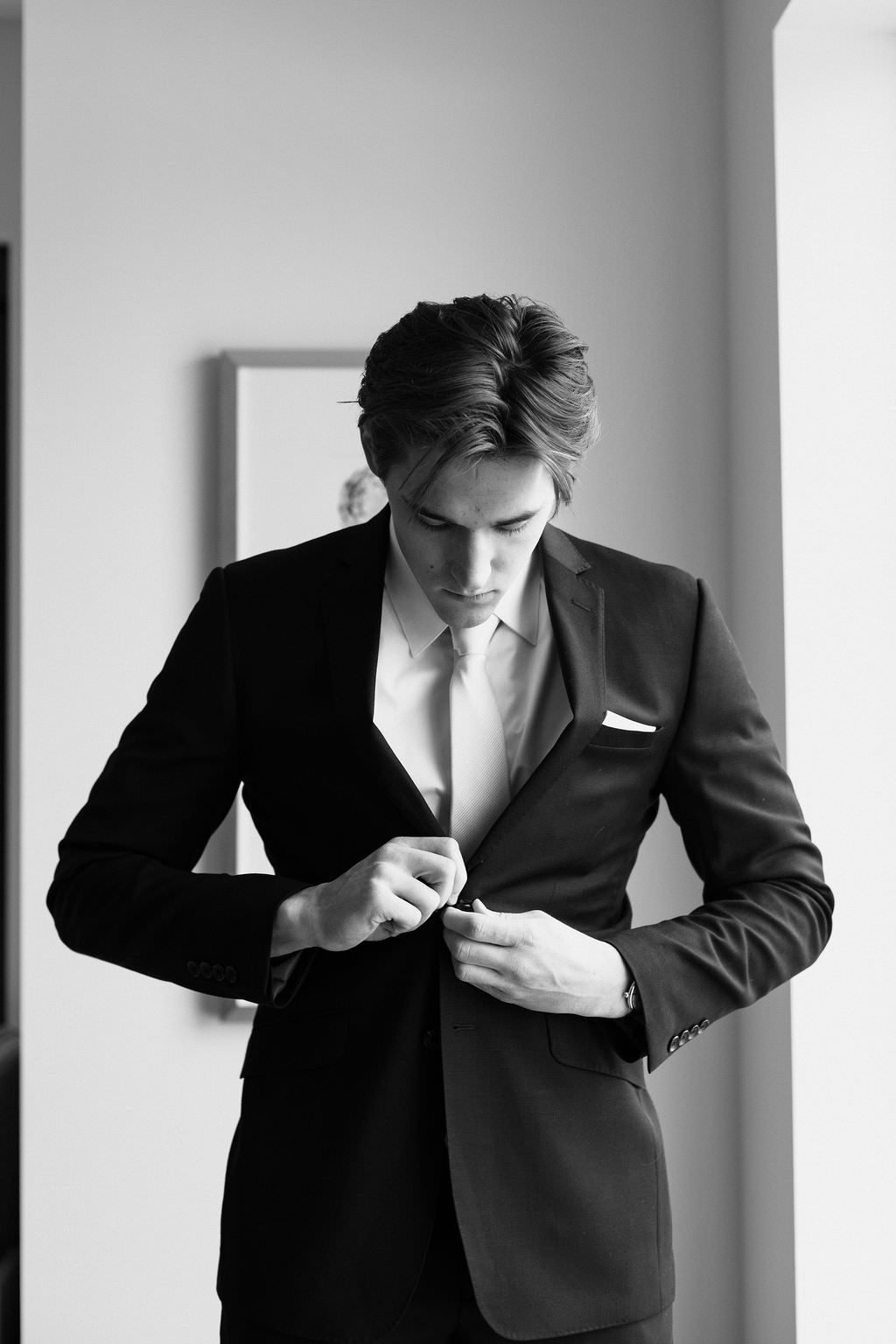 Black and white series showing groom adjusting suit jacket in preparation.