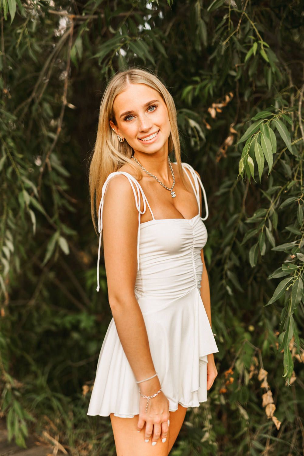 Outdoor summer portrait with lush green foliage and white sundress.