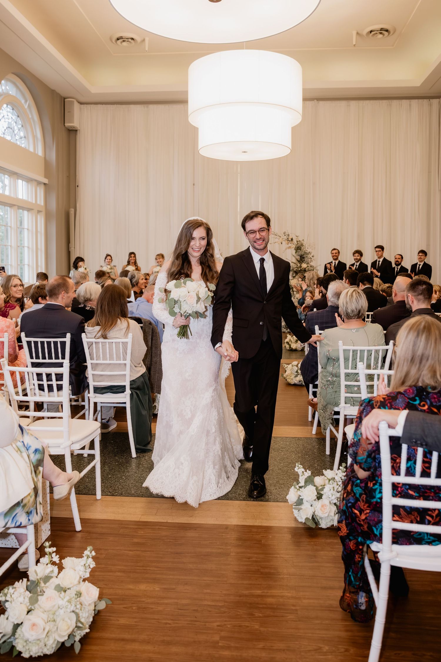 Bride and groom walk down the aisle smiling after wedding ceremony in elegant white draped venue.