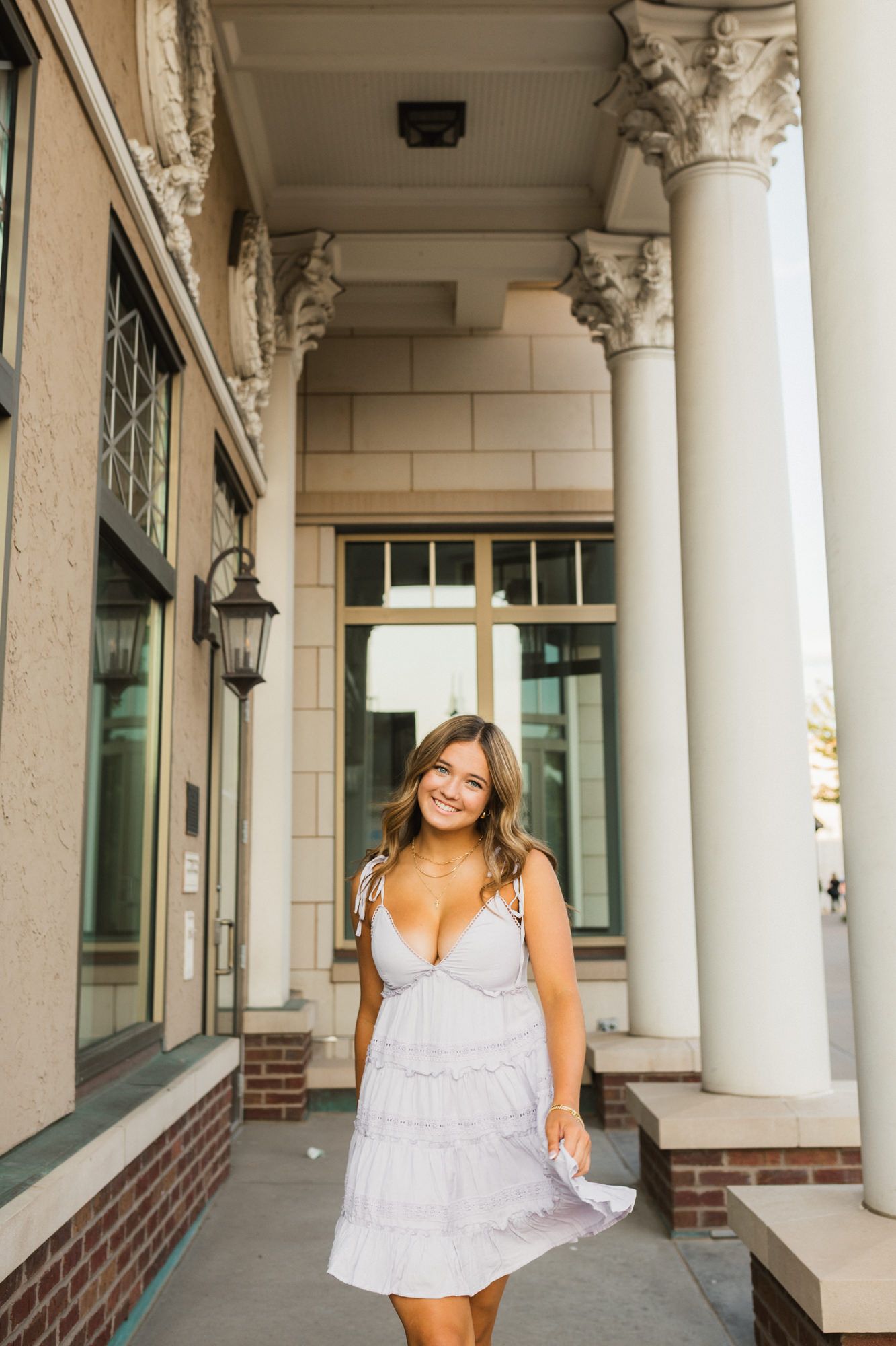 Smiling young woman in a white sundress posing by elegant white columns outside a classic building.