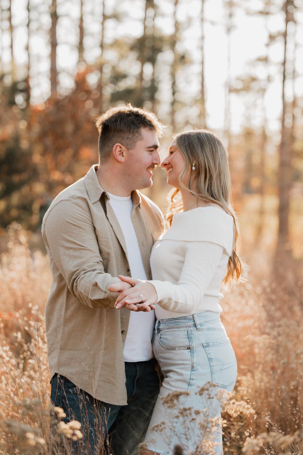 A romantic couple shares tender moments in a sunlit autumn field with tall grass and trees in the background.